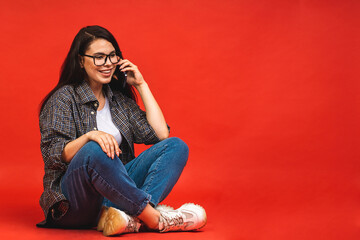 Canvas Print - Business concept. Portrait of happy smiling brunette woman in casual sitting on floor in lotus pose and using mobile phone isolated over red background.