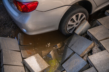 Wall Mural - The car fell into a huge sinkhole on broken pavement road surface on which cars park. Accident situation on a city street due to cracks in asphalt. Broken pavement hole with muddy water.