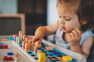 baby girl playing with different color wooden elements making tasks for education and brain exercise
