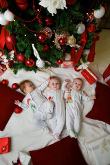 three babies are lying in a festive outfit on the background of new year and christmas decorations. The concept of holidays