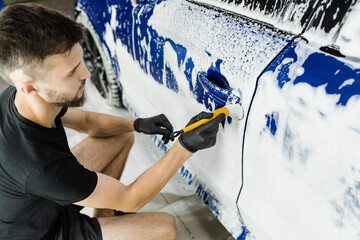 Wall Mural - Hand brush washing of car body with foam in car detailing service. Car wash worker washes a car body.