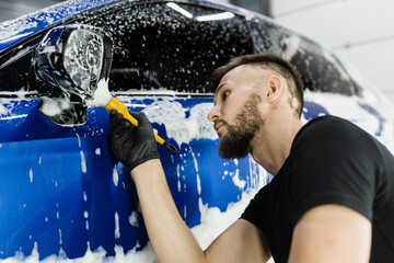 Wall Mural - Hand brush washing of car side mirror with foam in car detailing service. Car wash worker washes auto body.