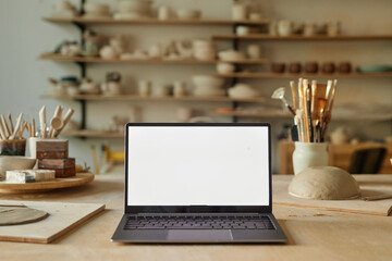 Background image of opened laptop with blank white screen in pottery workshop, copy space