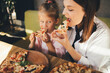© polinaloves - Mother and daughter eat pizza in a cafe.