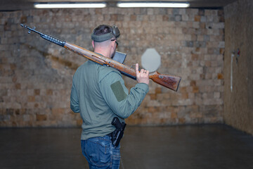 A man with an old rifle from the Second World War in a shooting range, view from the back.