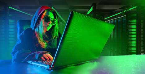 Woman programmer. Laptop on desk hacker girl. Female in hooded sunglasses. Programmer uses computer for hacking. Woman with laptop in server room. Concept of hacking servers. Professional programmer