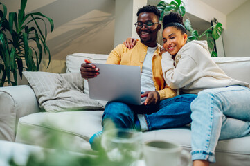 Multiracial couple using laptop while sitting on a sofa at home