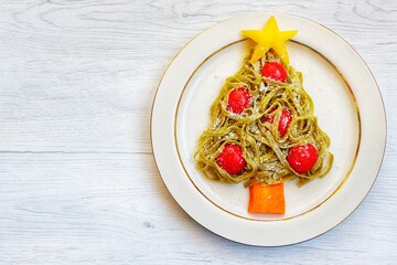 Wall Mural - Christmas tree pasta made it from spinach tagliatelle pasta,tomatoes,carrot,parmesan cheeses and yellow bell peppers on plate with white wood background.Creative art food idea for Christmas's dinner