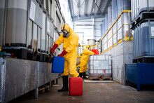 Providing Acids And Chemicals For Galvanizing In Metal Factory. Workers In Yellow Protective Suit And Gas Masks Holding Plastic Canisters With Aggressive Materials.