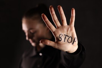 Woman with word Stop written on hand against dark background, closeup. Domestic violence concept