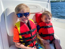 Young Brothers Riding In Boat In Bay Wearing Life Jackets
