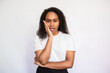 Portrait of distrustful young woman looking at camera. African American lady wearing white T-shirt standing with bored expression over white background. Boredom and distrust concept