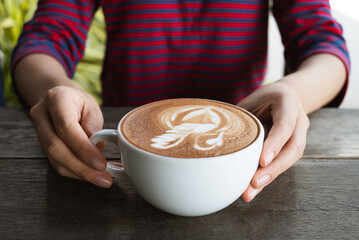 Wall Mural - Latte art coffee with swan shape in coffee cup holding by hand ready to drink