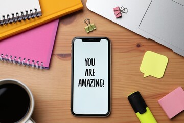 Wall Mural - Smartphone with phrase You Are Amazing on screen and stationery against wooden background, flat lay