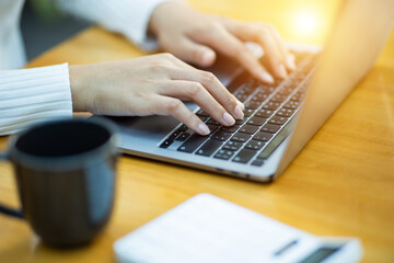 Wall Mural - Close-up of a woman's hand typing on a laptop. coffee cup on table A woman uses a laptop while sitting at a table in a cozy cafe.