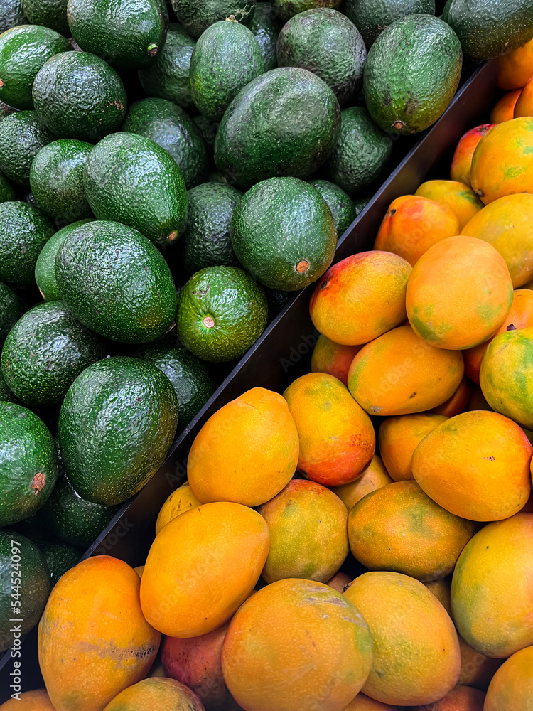 Tasty avocados and mangoes as background