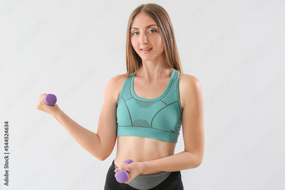 Sporty young woman with dumbbells on light background