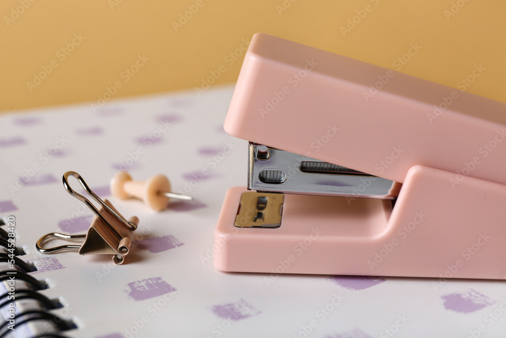Office stapler and notebook on color background, closeup