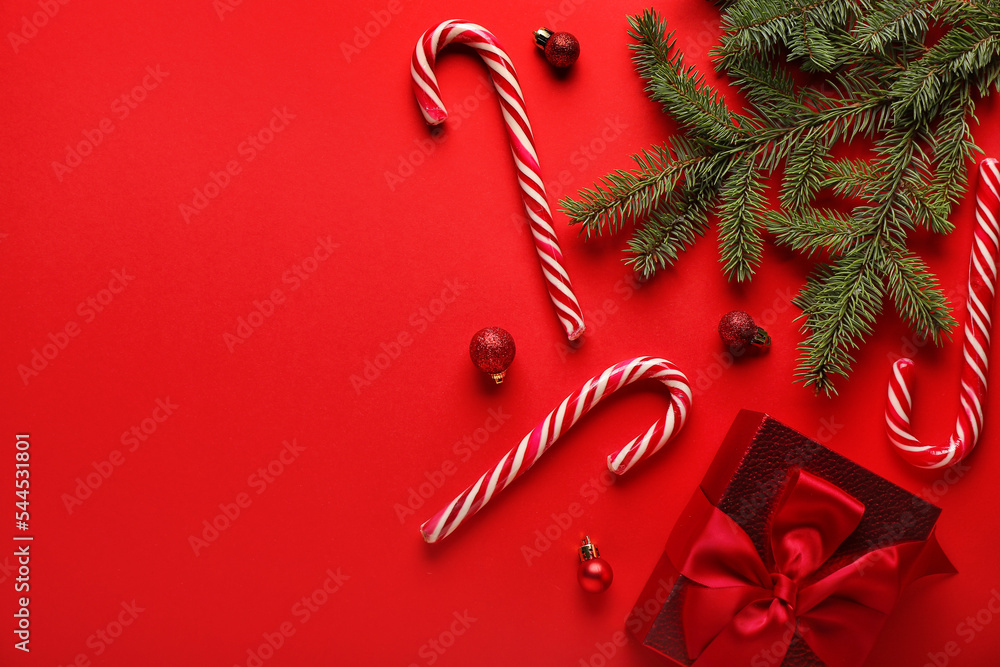 Candy canes with Christmas balls, gift and fir branches on red background