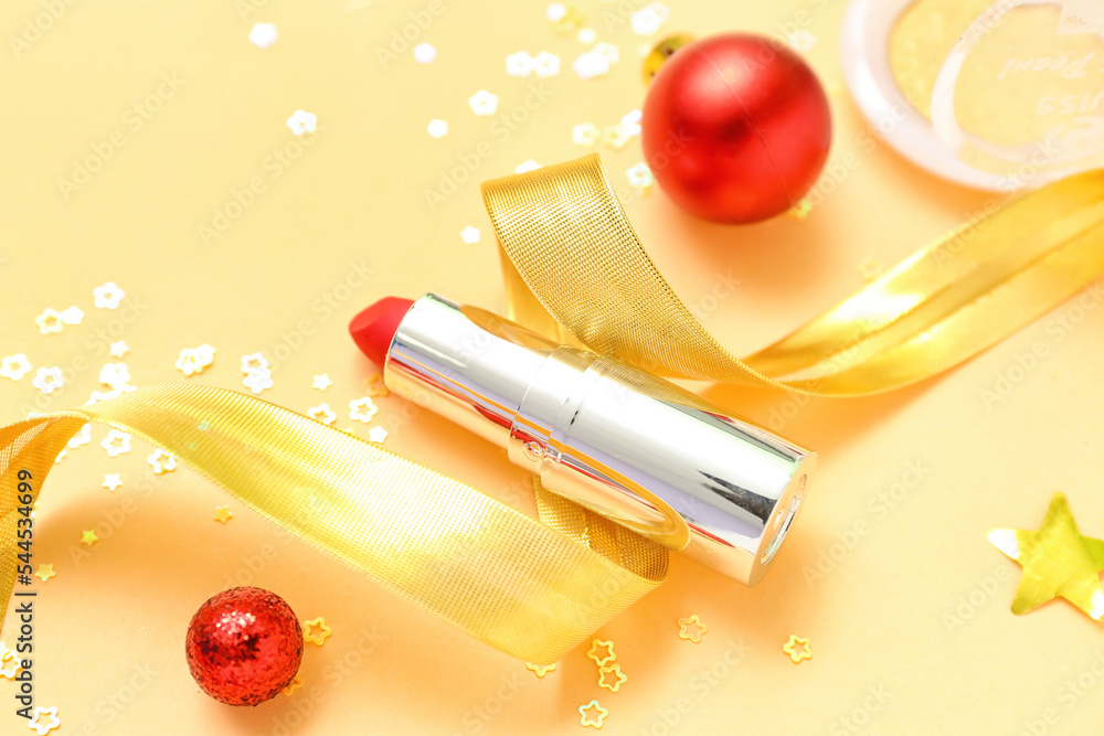 Red lipstick with Christmas decor on yellow background, closeup