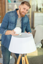 Young Man Changing Light Bulb At Home