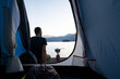 Aube à travers l'ouverture d'une tente de camping sur un paysage de lac entouré de montagnes à l'automne en Italie avec un jeune homme en contemplation