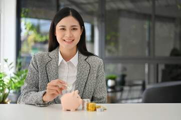 Sticker - Attractive Asian businesswoman insert coins in a pin piggy bank on the table.