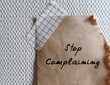 Torn paper stick on wallpaper with handwriting STOP COMPLAINING, remind oneself to complain less and instead fixing a problem, complainers can be draining, annoying, frustrating