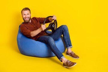 Poster - Full size portrait of overjoyed guy sit bag arms hold wheel have good mood isolated on yellow color background