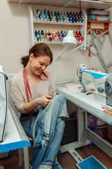 Wall Mural - A woman mends jeans, sews a patch on a hole in the home studio.Mending clothes concept,reusing old jeans.Small business.