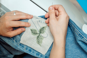 Wall Mural - A woman mends jeans, sews a patch on a hole, hands close-up.Mending clothes concept,reusing old jeans.