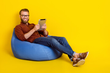 Poster - Full size portrait of clever person sit comfort bag hold use tablet isolated on yellow color background