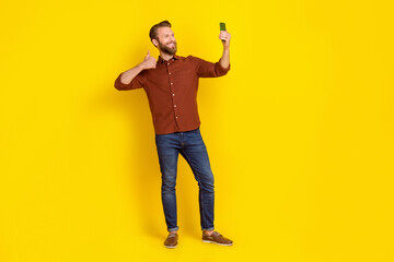 Wall Mural - Full body of positive attractive guy hold telephone take selfie show thumb up isolated on yellow color background