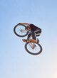 © Michael C/peopleimages.com - Mountain bike, speed and sports with a man jumping in the air during a race outdoor against the sky from below. Blue sky, energy and bicycle with a professional male biker or athlete in action