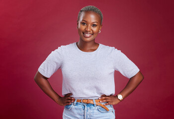 Poster - Young, african woman and hands on hips in studio for beauty, fashion and style with happiness. Happy black woman, portrait pose or smile face against red background for cosmetics, makeup or glow skin