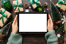 Christmas Online Shopping From Home, Female Hands Holding Tablet Pc With Blank White Display Top View. Woman Hand Holding Tablet With Blank Screen, Christmas Tree And Gifts On Background