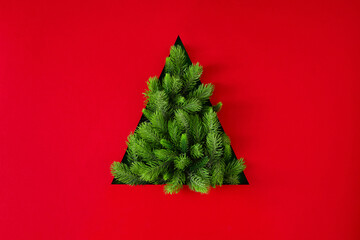 christmas tree silhouette made of fir branches on red background. flat lay. new year minimal concept