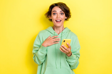 Photo portrait of lovely young woman hold telephone impressed point self lottery wear trendy green look isolated on yellow color background