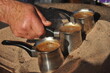 Arabic coffee brewed in a brass metal crucible in hot sand on one of the street stalls in Aqaba, Jordan. Aroma of coffee with cardamom and sugar for 1 Jordanian dinar.