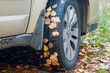Koła samochodu osobowego. Opony oblepione śliskimi, jesiennymi, żółtymi liśćmi. Poślizg na liściach zalegających pobocza.