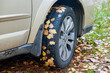 Koła samochodu osobowego. Opony oblepione śliskimi, jesiennymi, żółtymi liśćmi. Poślizg na liściach zalegających pobocza.