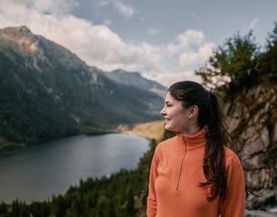 Wall Mural - Woman hiker on the top of the mountain. Concept of adventure vacations. Traveler millennial girl is staying on the cliff edge with autumn forest and enjoying beautiful valley view.