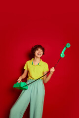 Portrait of cheerful teen girl with curly brown short hair posing with vintage phone isolated over red background. Having fun