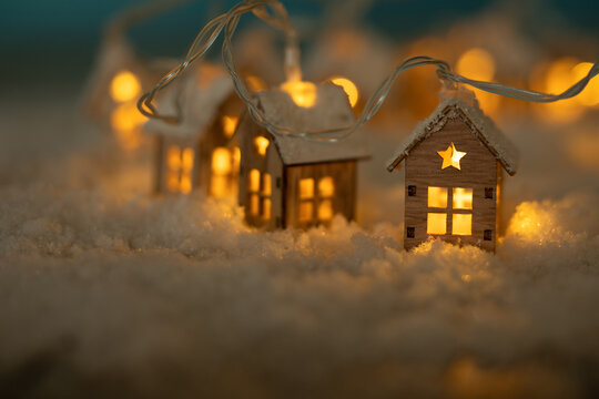 Fototapete - Abstract Christmas Winter Greeting Card with Wooden Houses Christmas String Lights in Cold Snow Landscape and Glowing Golden Lights in Background. Christmas or Energy themes.