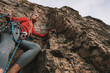 © Cavan Images - A woman in a red shirt rock climbing on a sunny day.