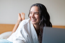 Happy Woman Surfing Internet On Laptop In Bedroom At Home