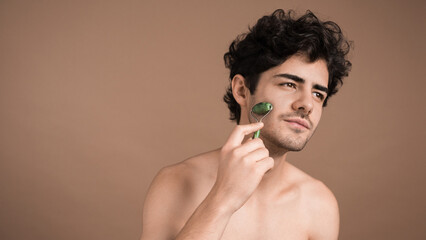 A young caucasian man with stubble beard is doing a facial massage using a roller