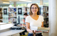 Joyful Young Latin Female Reading The Book While Standing In Library During Daytime