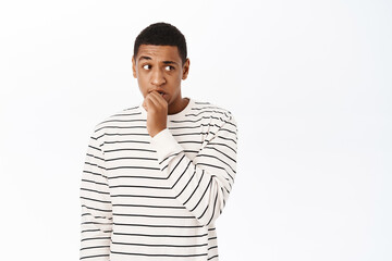 Wall Mural - Anxious middle aged african american man, biting fingers, looking scared or nervous, standing over white background