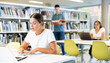 © JackF - Positive young lady in casual clothes working remotely using a computer in a quiet library